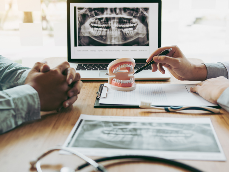 A dentist and patient discussing dentures at a table with paperwork