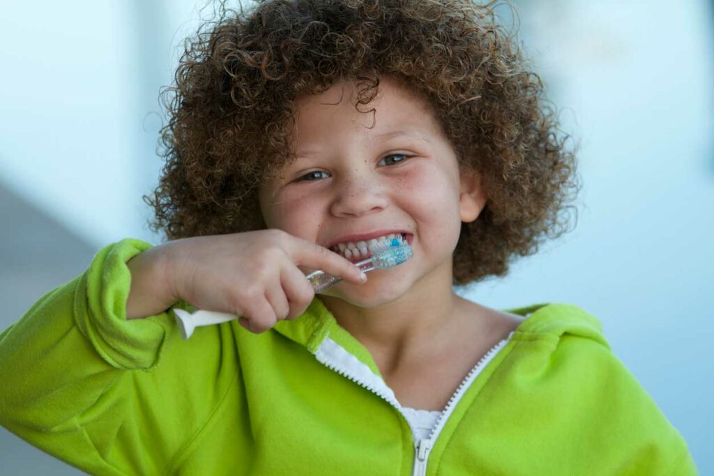 child smiling while brushing their teeth