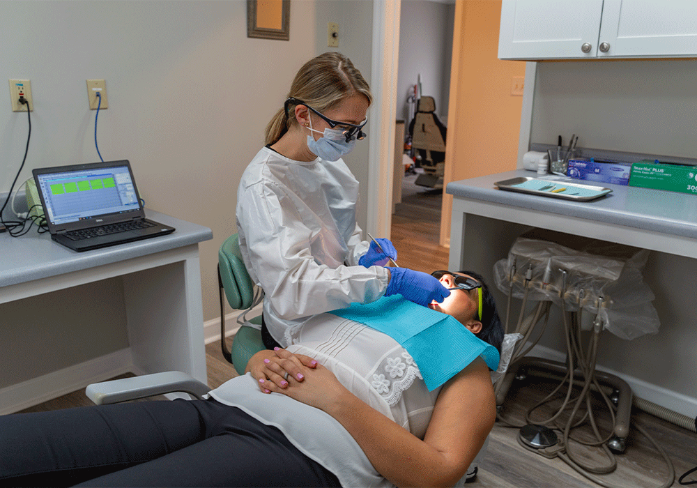 dental assistant working on patient that is laying in exam chair